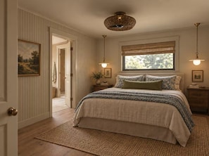 A bedroom with a bed, a window with a view, a door, and a hanging light fixture.