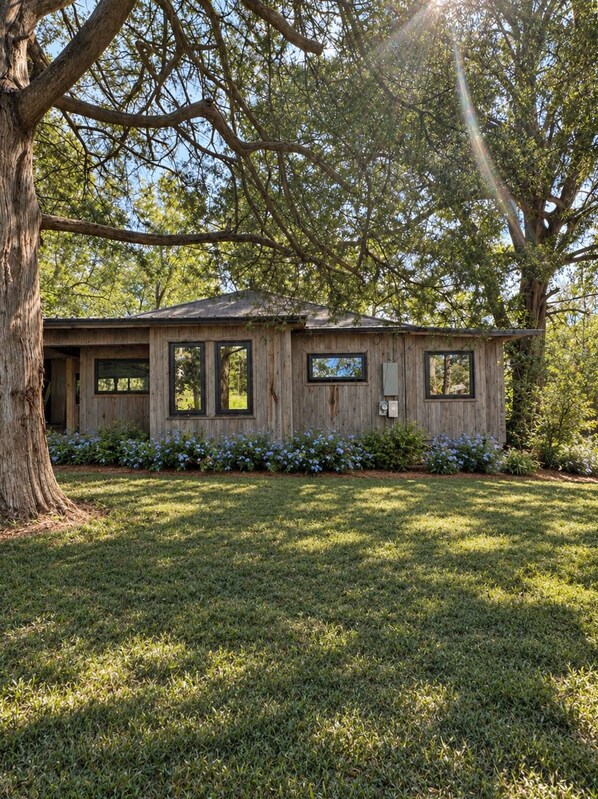 A wooden cabin with a sloped roof, surrounded by a well-maintained lawn and a large tree.