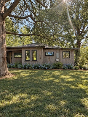 A wooden cabin with a sloped roof, surrounded by a well-maintained lawn and a large tree. - The Pecan House, A 3BR Restored Cottage in Woodville (Woodville)