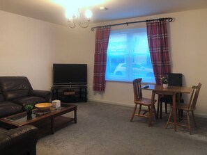 A living room with a flat-screen TV, leather sofa, wooden coffee table, and a dining area with a table and chairs. - Cosy flat 1 min from Union Street, perfect for 2 or a small family (Aberdeen)