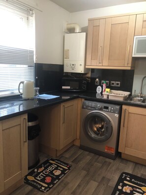 A compact kitchen with a washing machine, microwave, and a water heater. - Cosy flat 1 min from Union Street, perfect for 2 or a small family (Aberdeen)