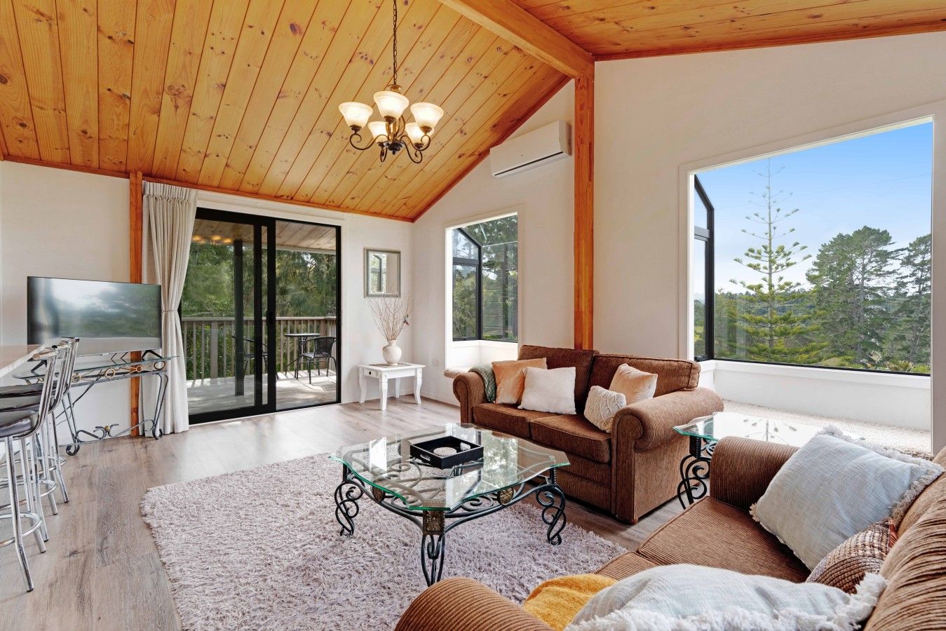 A spacious living room with a wooden ceiling, a sofa set, a glass coffee table, and a TV.