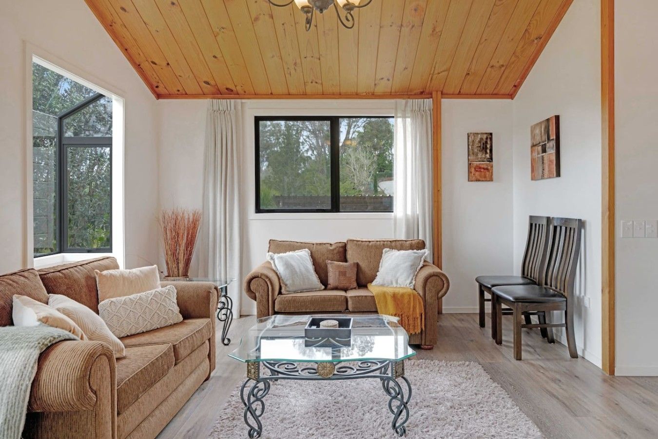 Ein Wohnzimmer mit Holzbalkendecke, zwei Sofas, einem Glastisch und einem Essbereich mit einem Stuhl.