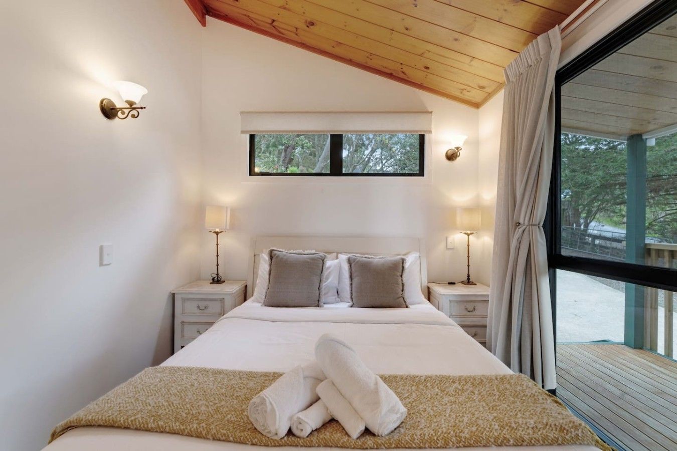A bedroom with a large bed, two bedside tables with lamps, a window with curtains, and a view of the outdoors.