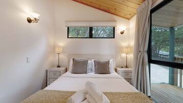 A bedroom with a large bed, two bedside tables with lamps, a window with curtains, and a view of the outdoors.