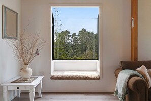 A room with a window seat, a white table with a vase, and a brown sofa.
