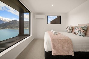 Ein Schlafzimmer mit einem großen Fenster, einem Bett mit blumigen Kissen und Blick auf Berge und Wasser.