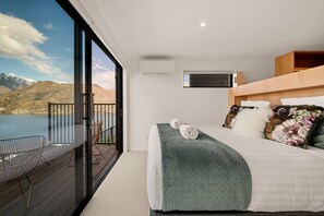 A bedroom with a large bed, a balcony with a chair, and a view of mountains. - Snowy Place by Sothebys Luxury Rental Homes (Queenstown)