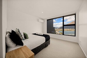 A bedroom with a large window, a bed, and a wooden nightstand. - Snowy Place by Sothebys Luxury Rental Homes (Queenstown)