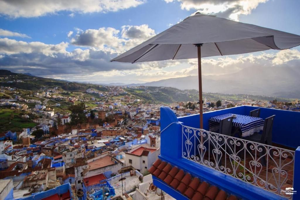 Varanda com guarda-sol branco, com vista para uma cidade densamente povoada e telhados de terracota.