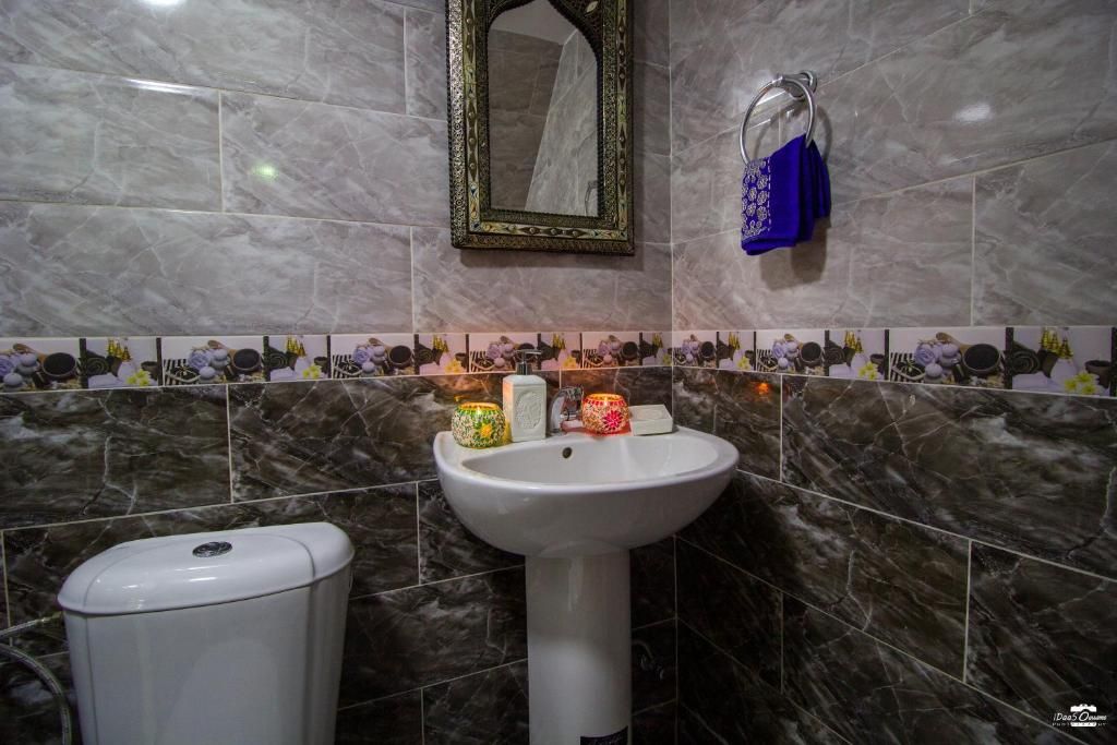 A bathroom with a white pedestal sink, a mirror with an ornate frame, and a toilet.