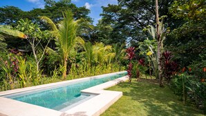 A rectangular swimming pool with a clear blue water surface, surrounded by a well-maintained grassy area and various tropical plants. - Lapas · Jungle House for 4 + Pool +AC · Walk to Beach · Cabuya (Cabuya)