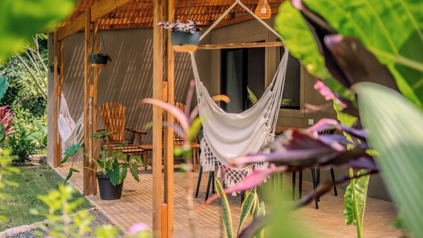 A hammock chair suspended from a wooden structure, with a view of a covered outdoor seating area and potted plants. - Lapas · Jungle House for 4 + Pool +AC · Walk to Beach · Cabuya (Cabuya)