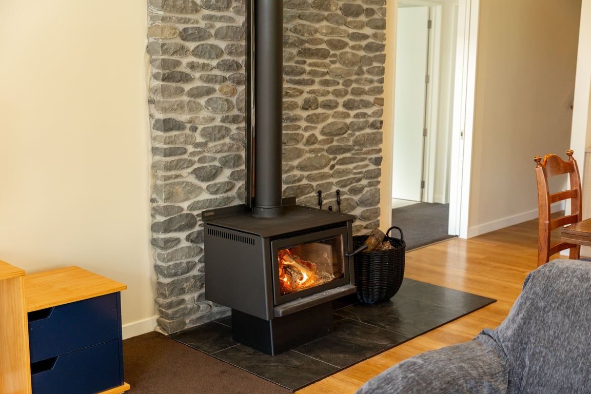 A room with a stone wall, a black wood-burning stove, a wooden chair, and a blue cabinet.
