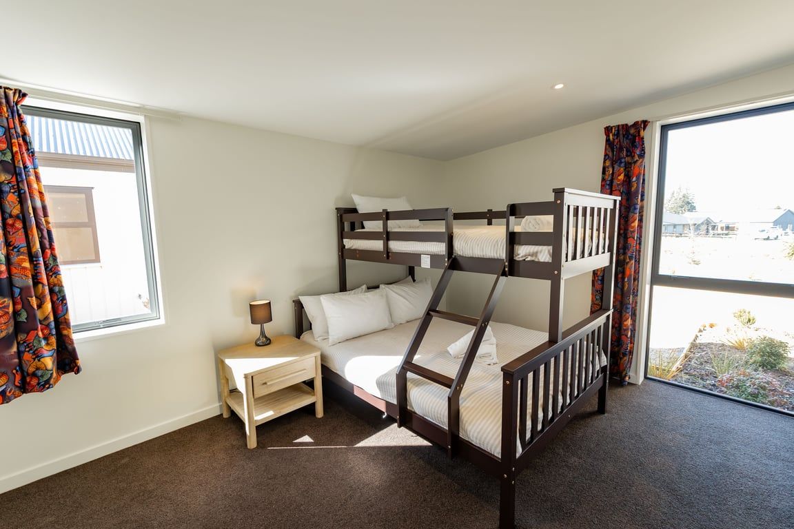 A bunk bed room with a window, a bedside table, and a view of the outside.