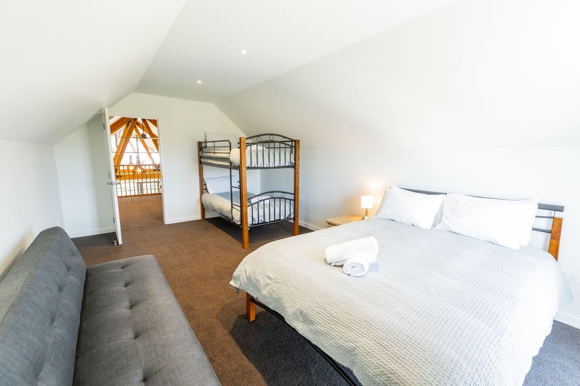 A bedroom with a bunk bed, a single bed, a sofa, and a nightstand with a lamp.