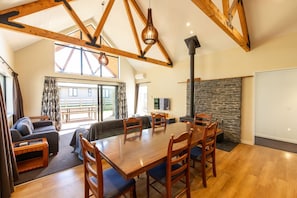 A spacious living area with a wooden dining table, comfortable seating, and a stone fireplace. - Riverside | BBQ & Fireplace | Reserve - HS519D (Hanmer)