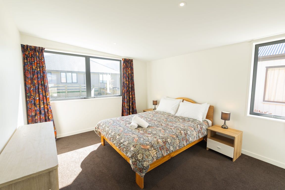 A bedroom with a large bed, two bedside tables, a nightstand, and a window with curtains.