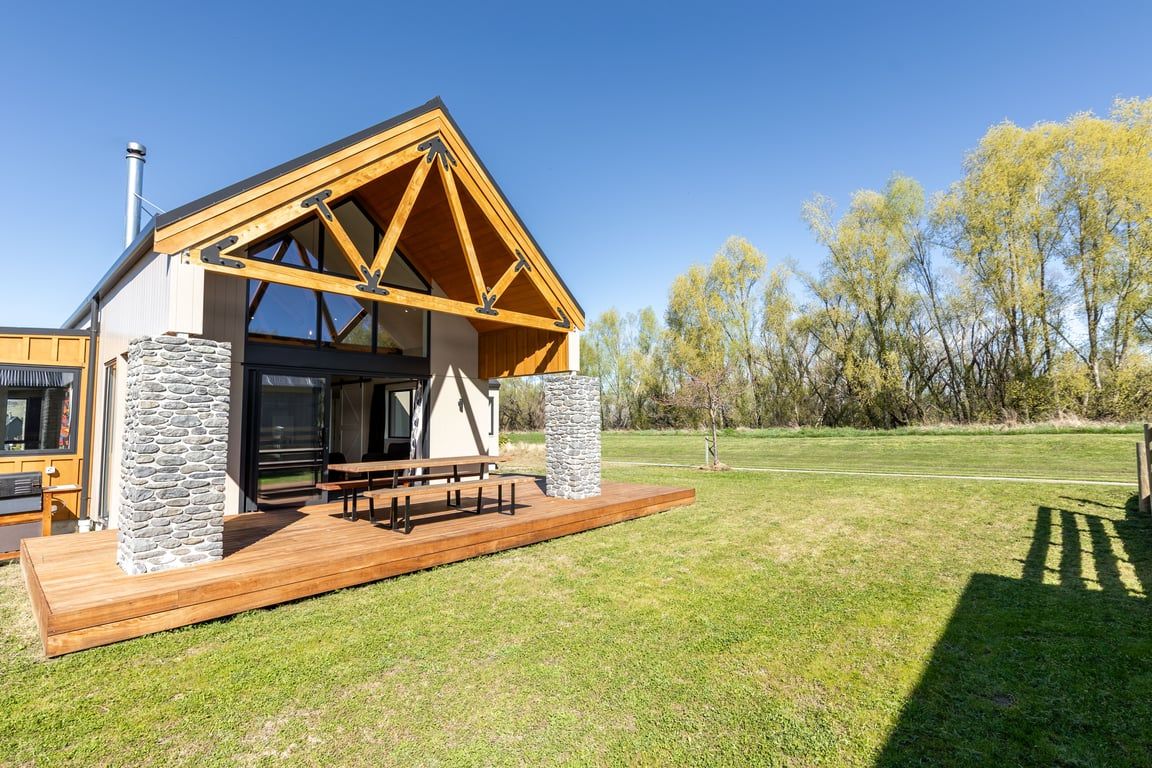A modern building with a wooden roof structure, stone pillars, and a wooden deck with benches.