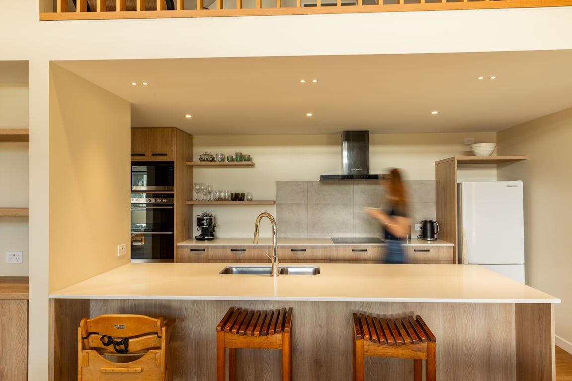 A modern kitchen with a central island, wooden bar stools, and a person in motion.