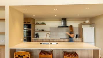 A modern kitchen with a central island, wooden bar stools, and a person in motion.