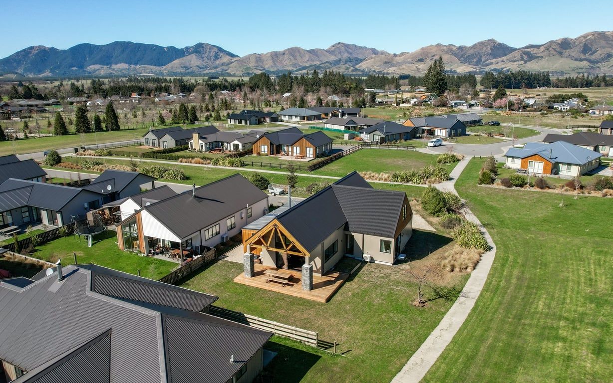A residential area with houses featuring modern architecture, surrounded by a well-maintained lawn and a mountain backdrop.