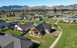 A residential area with houses featuring modern architecture, surrounded by a well-maintained lawn and a mountain backdrop. - Riverside | BBQ & Fireplace | Reserve - HS519D (Hanmer)