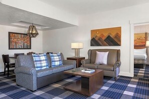 Een woonkamer met een bank, een salontafel, een lamp en een schilderij aan de muur.