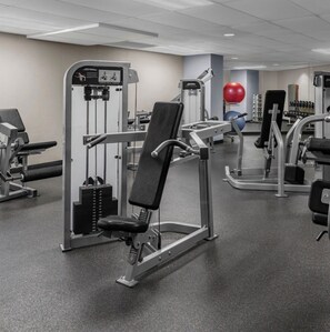 A gym with various exercise equipment including a bench press, a leg press, and a cable machine.