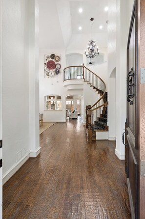 A spacious hallway with a wooden floor, a spiral staircase, and a wall adorned with clocks. - 5BR Frisco Retreat Near Universal Kids Resort/PGA (Frisco)