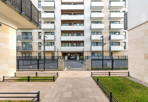 Un edifici residencial de diverses plantes amb balcons, una entrada tancada i un passeig pavimentat.