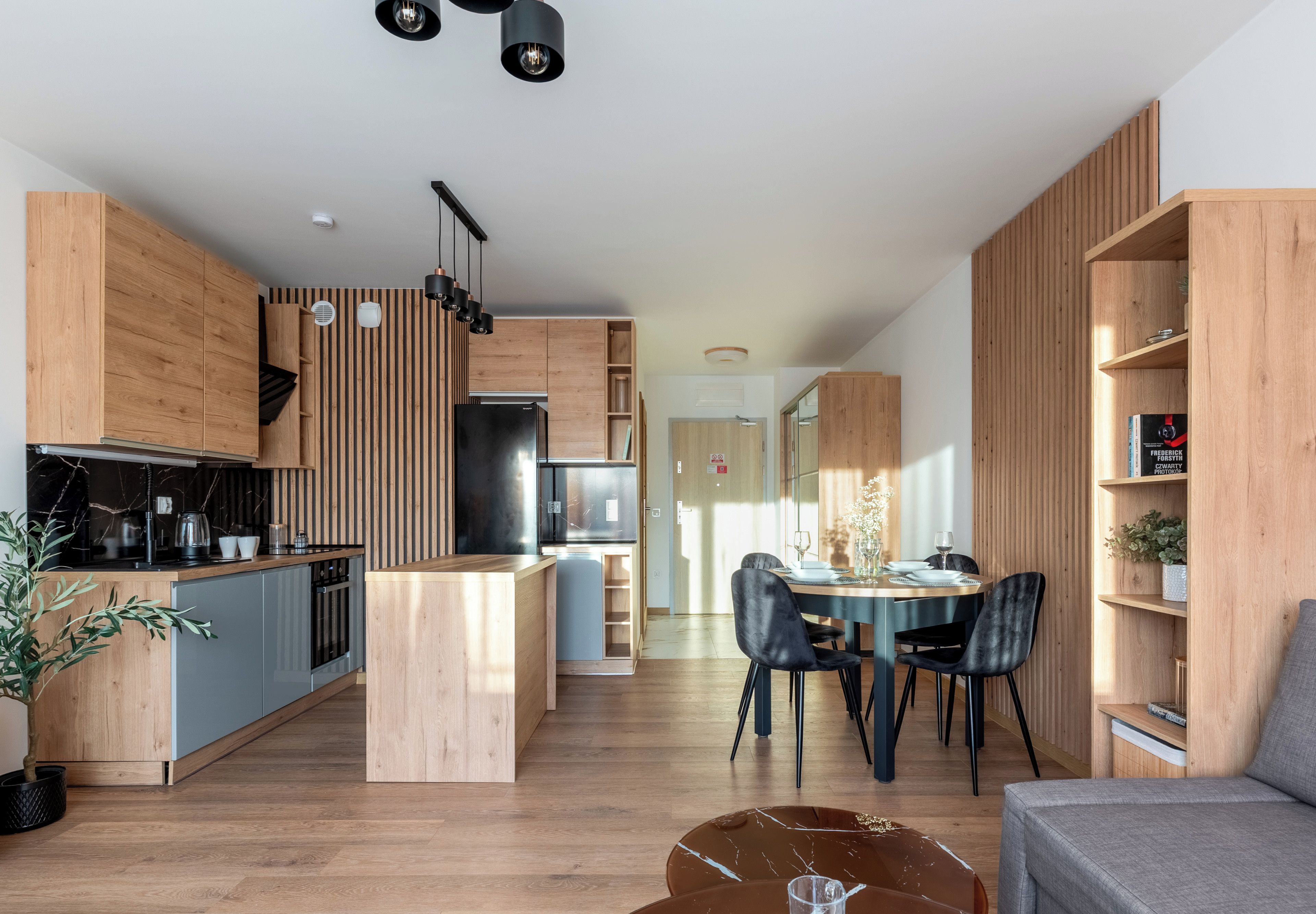 A modern kitchen with wooden cabinetry, a central island, and a dining area with a round table and chairs.