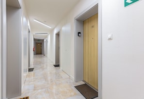 Un passadís d'hotel amb terra de marbre, portes i un extintor.