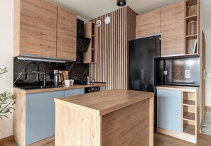 Eine moderne Küche mit Holzschränken, einem schwarzen Kühlschrank und einer Marmorarbeitsplatte.