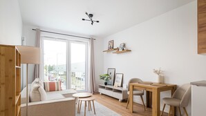 Una sala moderna con un sofá, una mesita redonda y una mesa de comedor con sillas. Hay un lámpara en el techo y vistas al exterior a través de amplias ventanas.