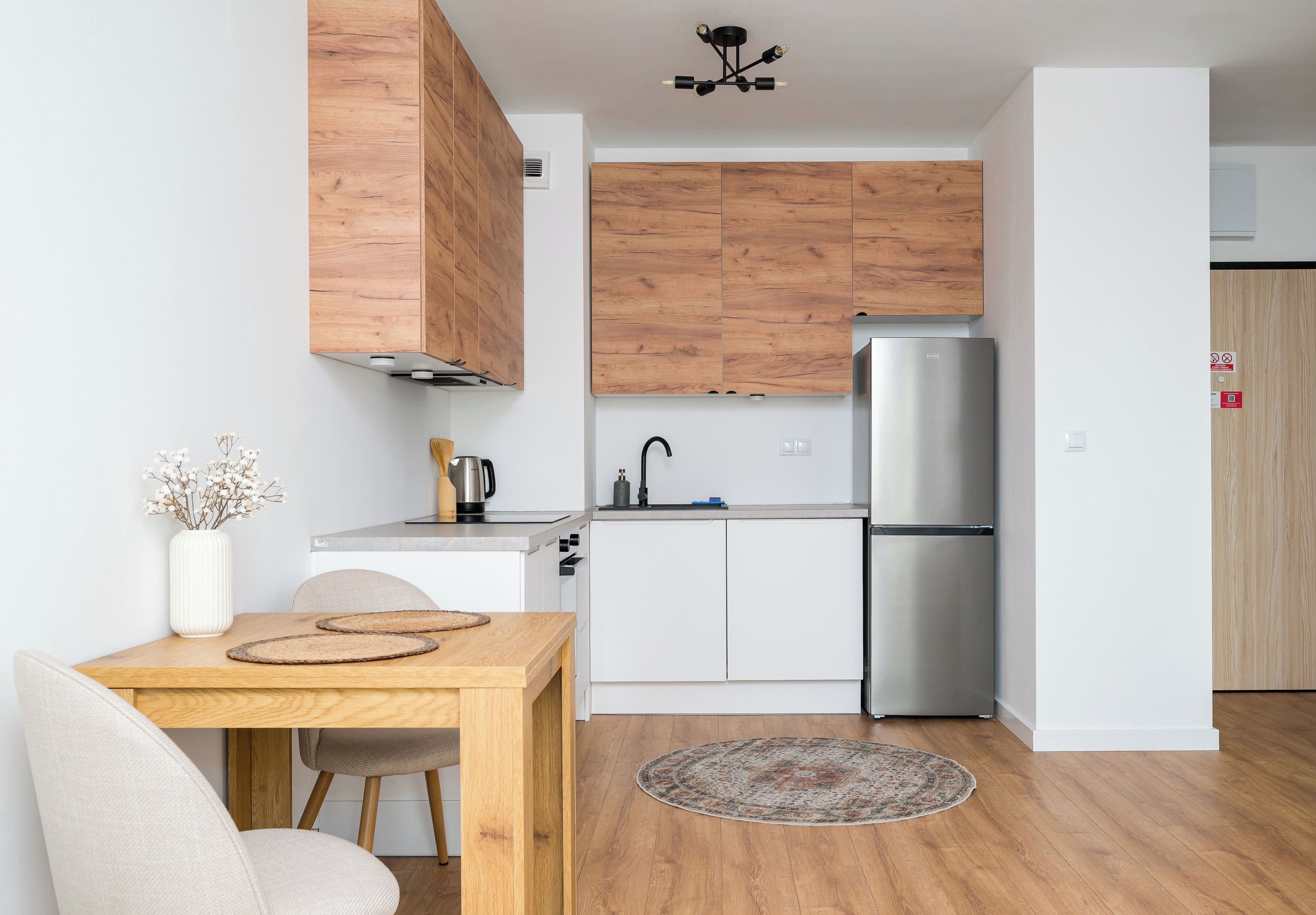 Una cocina moderna con armarios de madera, un refrigerador de acero inoxidable y un comedor con mesa y sillas.