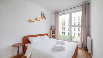Un dormitorio con una cama, una mesita de noche, una ventana con cortinas y vistas a edificios.