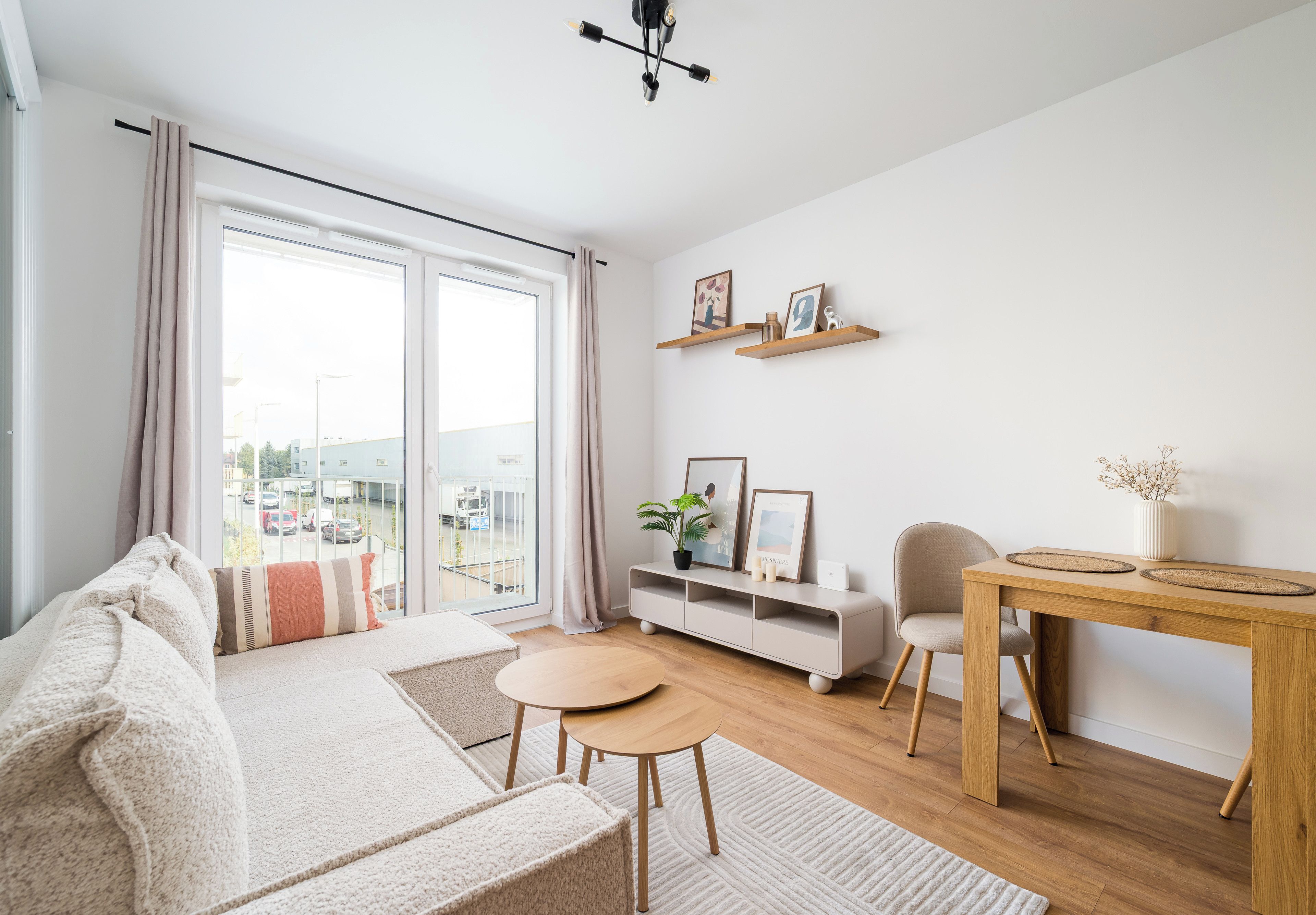 A modern living room with a sofa, a dining table, a chair, a TV stand, and a large window with curtains.