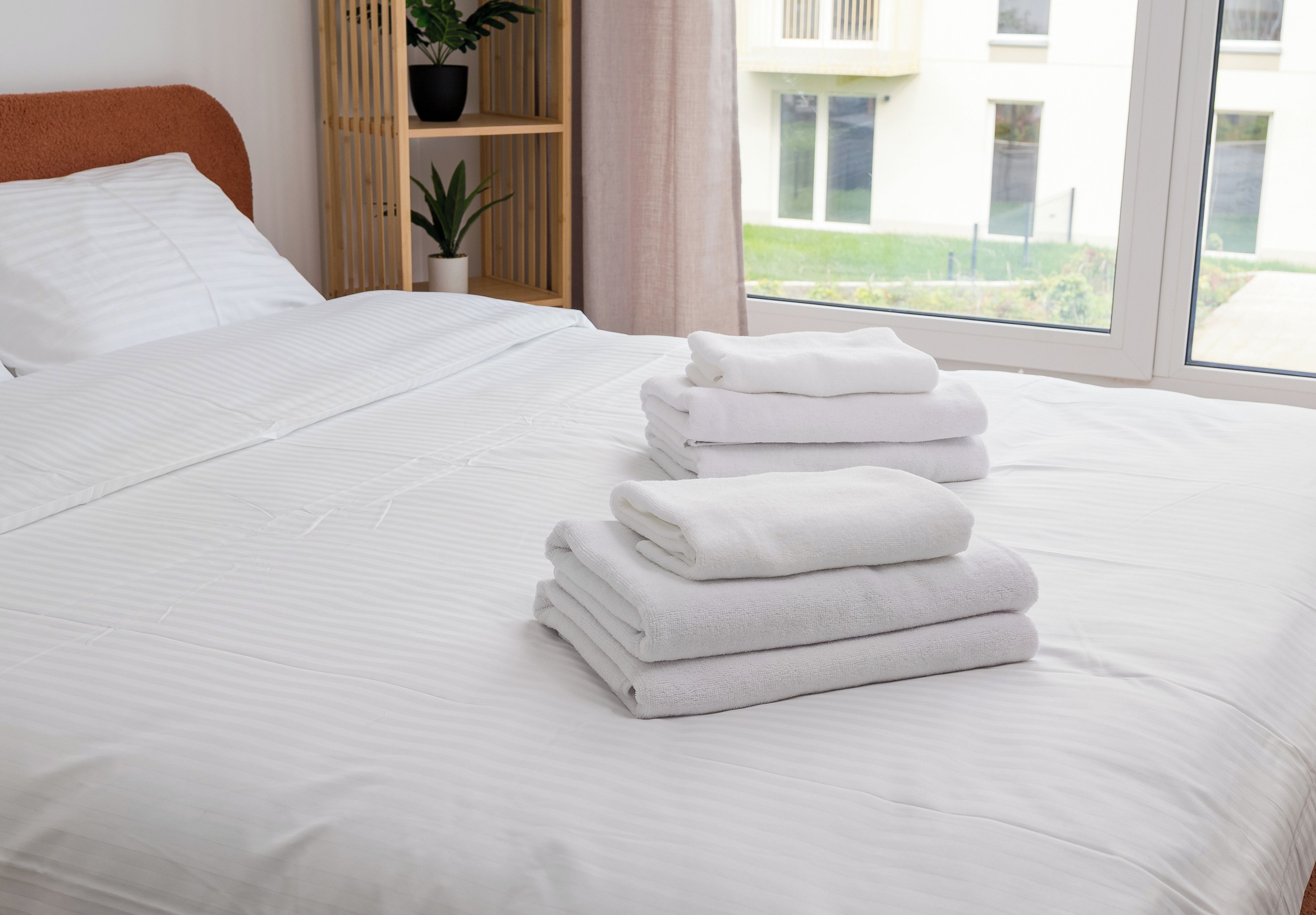 Una cama bien tendida con sábanas blancas y una pila de toallas dobladas.