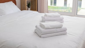 Una cama bien tendida con sábanas blancas y una pila de toallas dobladas.