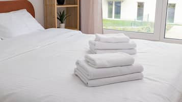 Una cama bien tendida con sábanas blancas y una pila de toallas dobladas.