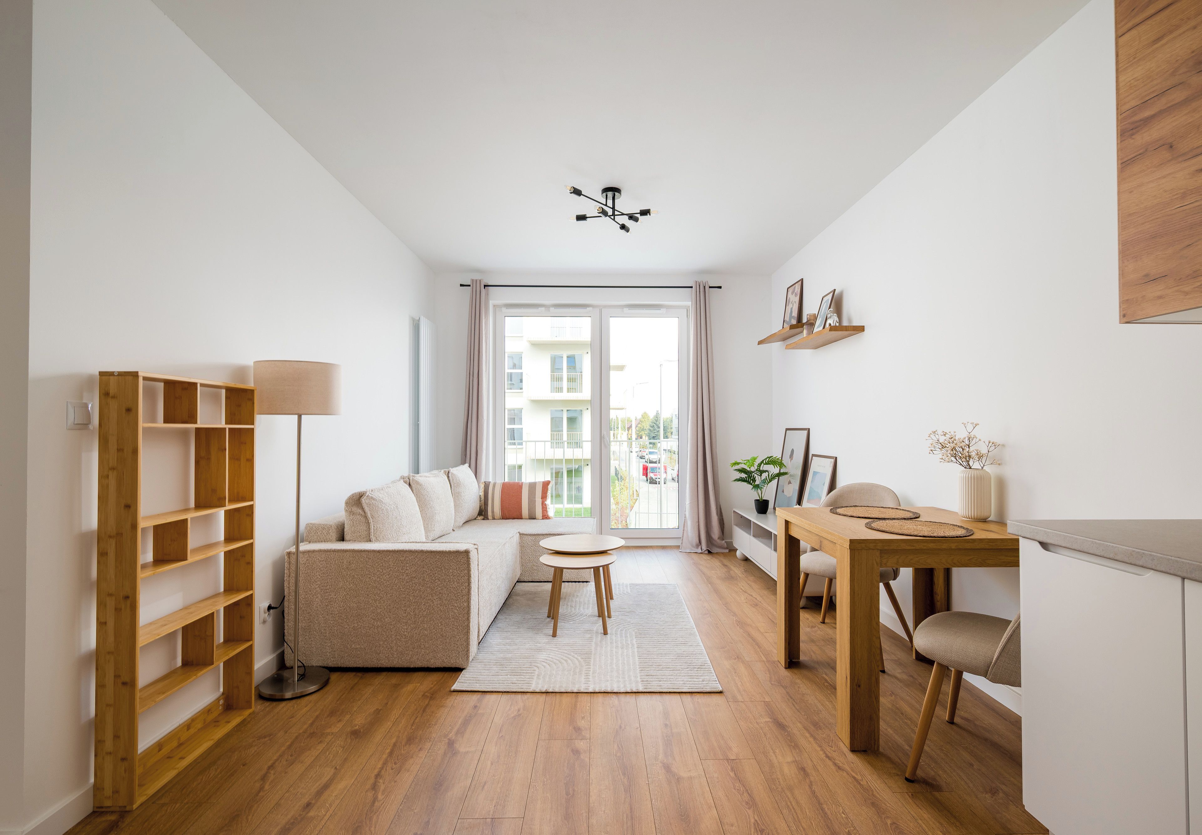 Ein modernes Wohnzimmer mit einer Couch, einem Esstisch mit Stühlen, einem hölzernen Bücherregal und einer Deckenleuchte.