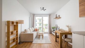 Ein modernes Wohnzimmer mit einer Couch, einem Esstisch mit Stühlen, einem hölzernen Bücherregal und einer Deckenleuchte.