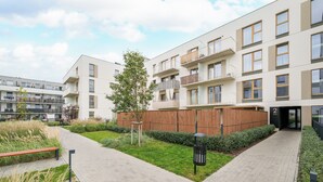 Un moderno edificio de apartamentos con un sendero pavimentado, un árbol pequeño y una cerca de madera.