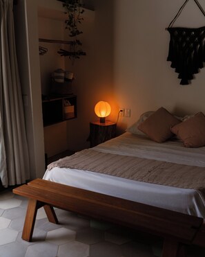 Ein Schlafzimmer mit Bett, Nachttisch, Lampe und einer hängenden Pflanze.
