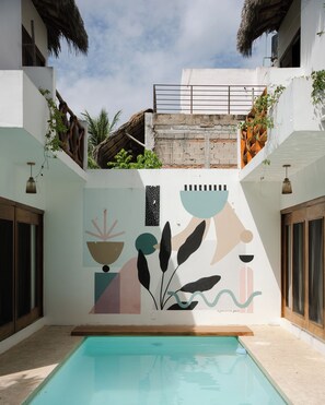 Ein Swimmingpool mit Wandmalerei, einem Reetdach und einem Balkon mit Pflanzen.