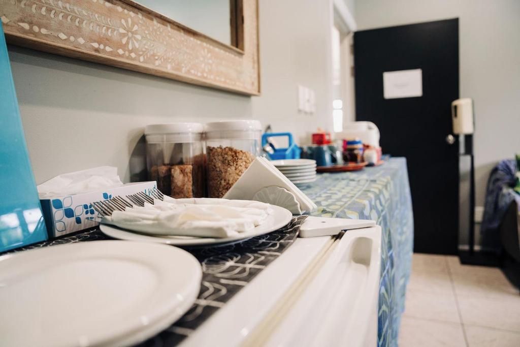 Habitación de hotel con zona de comedor que incluye una mesa con platos, tazones y una cafetera. Se ven recipientes con snacks y un espejo en la pared.