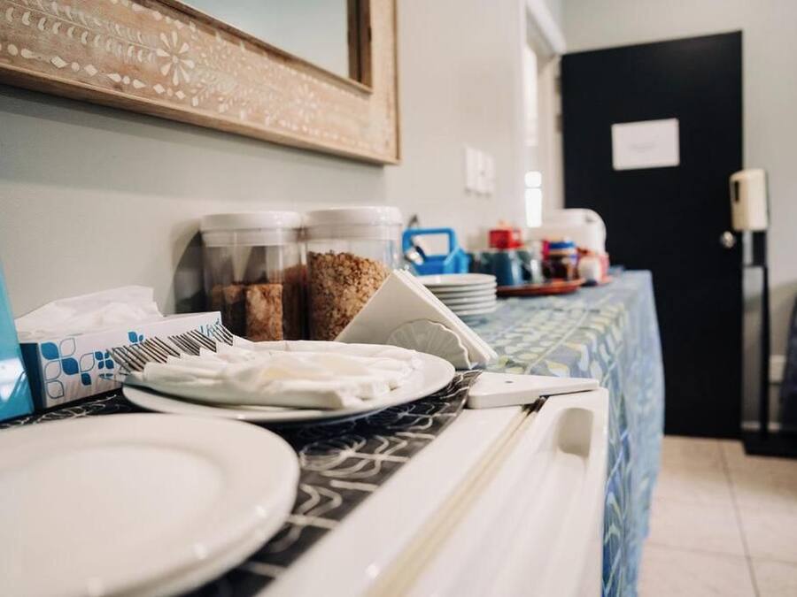 A hotel room with a dining area featuring a table set with plates, bowls, and a coffee maker. There are containers of snacks and a mirror on the wall.
