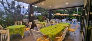An outdoor dining area with tables and chairs, surrounded by greenery and a pool. - Sands of Rarotonga (Avarua)