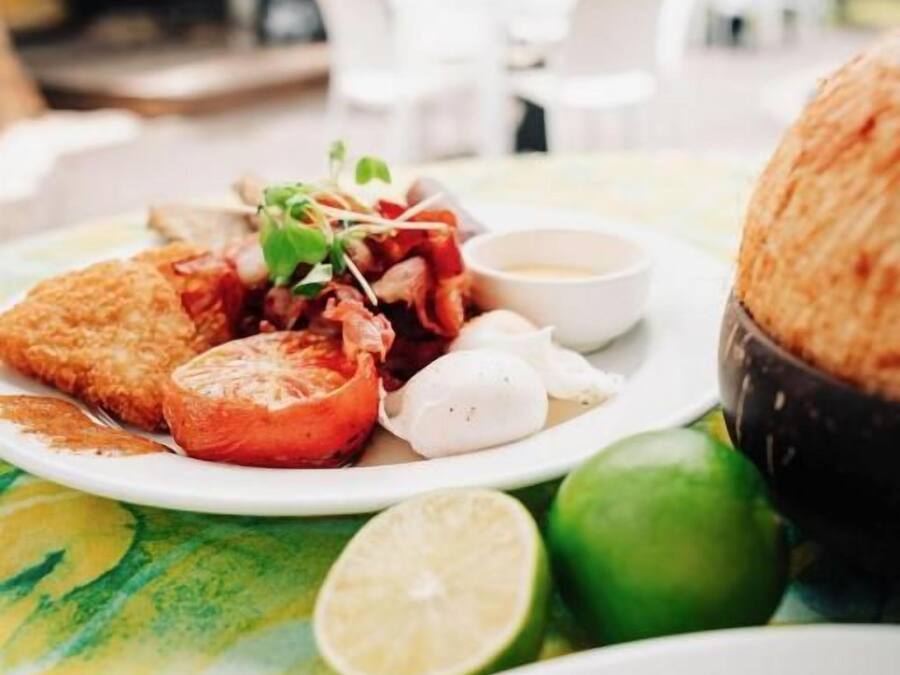 A dining table with a plate of food, including a breaded item, tomato slices, and a small bowl of sauce.
